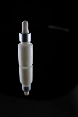 A white cosmetic bottle with an eyedropper lies on a glass table on a black backgroundの写真素材
