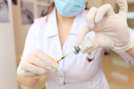 the cosmetologist holds a syringe with a bottle of the drug in front of him and draws a drug for beauty injections from itの写真素材