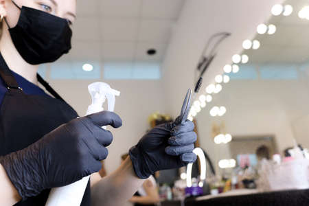 a girl who is a master of permanent makeup in a black mask and gloves holds a tattoo machine in her hands stands at the window and looks into itの写真素材