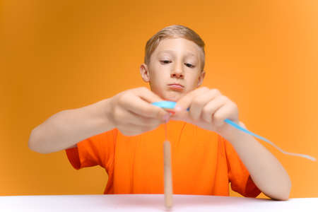 a child in an orange T-shirt sits at a table and twists thin paper strips on a quilling toolの写真素材