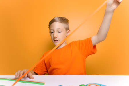 a child in an orange T shirt applies glue to a sheet of white paper to prevent the gluing of thin...