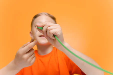 a child in an orange T shirt applies glue to a sheet of white paper to prevent the gluing of thin twisted strips made in the quilling techniqueの写真素材