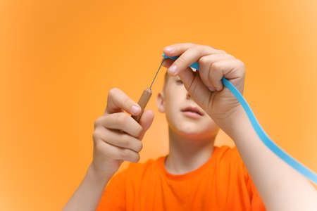 a child in an orange T shirt applies glue to a sheet of white paper to prevent the gluing of thin...