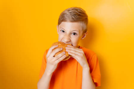 a boy in an orange T shirt holds a hamburger in one hand spreads his arms out to the sides and shows...