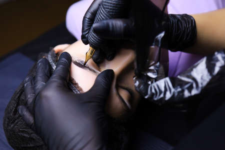 hands of a tattoo artist wearing black gloves holding a tattoo machine in one hand and a cotton...
