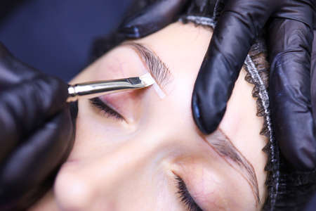 tattoo artist in black gloves with a tattoo machine for applying pigment to the client's eyebrowsの写真素材