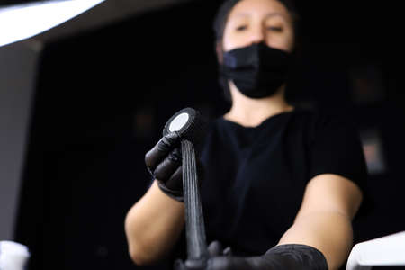 tattoo artist in a black uniform wrap the stretch tape around the tattoo machine for additional fixationの写真素材
