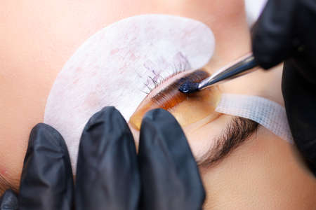 close-up of the master's hands apply paint with a brush to the cilia that are glued to the curling rollerの写真素材