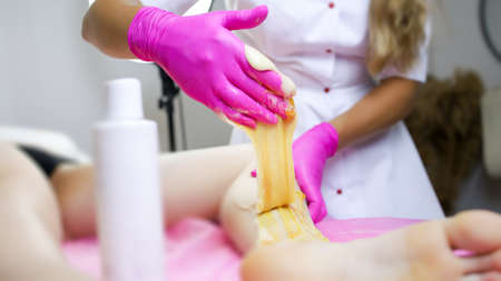 the master of sugar hair removal and removal of unwanted hair with wax stands in front of the client and works with the hand area removing unwanted hair on itの写真素材
