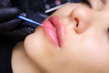 applying anesthesia to the model's lips with a small blue brush before the permanent makeup procedureの写真素材