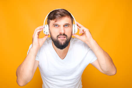 a man, tightly pressing musical headphones to his ears, and looking at the camera.の写真素材