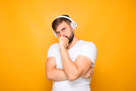 a man with white headphones listens to music and ponders, putting his hand to his face.の写真素材