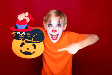 child with halloween make-up holds a cardboard pumpkin in his hands.の写真素材