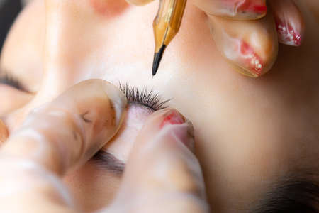 the tattoo artist holds the eyelids of the model with two fingers and makes a tattoo between the ciliaの写真素材
