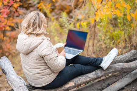 a beautiful girl in a beige down jacket sits on the logs of an autumn park