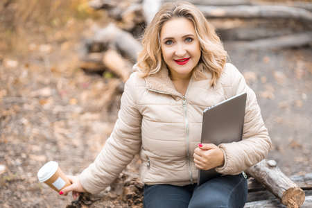 a beautiful girl in a beige down jacket sits on the logs of an autumn parkの写真素材