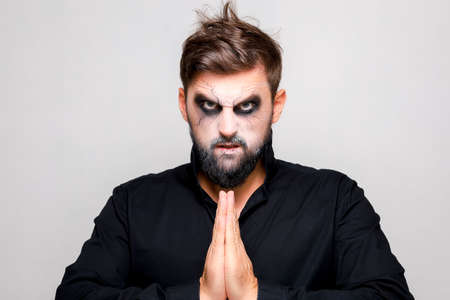 a man with undead makeup for Halloween holds his hands in front of him and looks at the camera from under his foreheadの写真素材