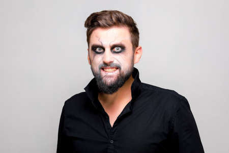 a man with undead makeup for Halloween holds his hands in front of him and looks at the camera from under his foreheadの写真素材