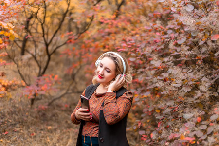 a young woman on the background of an autumn park with headphones listening to musicの写真素材