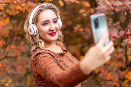a young woman on the background of an autumn park with headphones listening to musicの写真素材