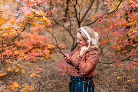 a young woman on the background of an autumn park with headphones listening to music