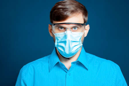 A doctor in a medical mask and gloves, in a blue uniform, shows a thumb upの写真素材