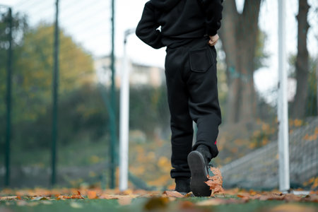the boy, who is wearing a black hooded jacket, holds an autumn leaf in his hand.