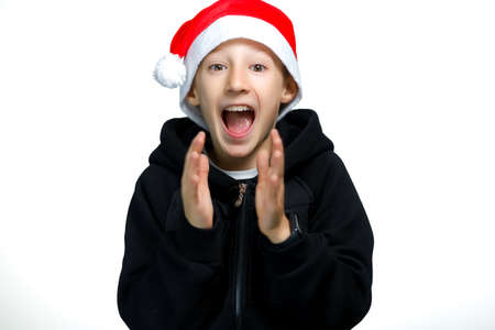 a boy in a red Santa hat who stands on a white background gives a thumbs up and laughs loudlyの写真素材