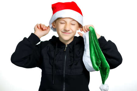a cheerful boy in a red Santa hat stands on a white background and laughs merrilyの写真素材