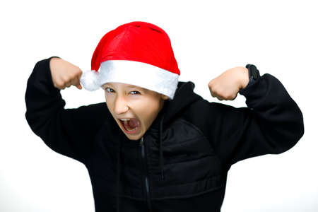a cheerful boy in a red Santa hat stands on a white background and laughs merrilyの写真素材