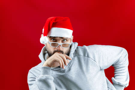 a bearded man in a Santa Claus Christmas hat on a red background imitates an air kissの写真素材