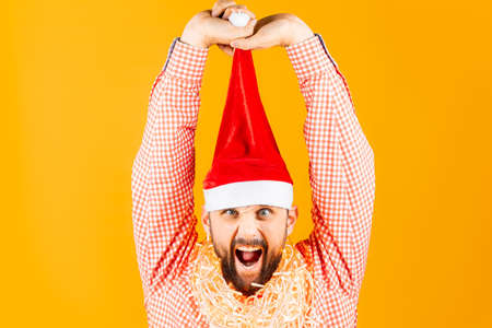 a man in a red plaid shirt on a yellow background pulls the New Year's caps of Santa Claus upの写真素材