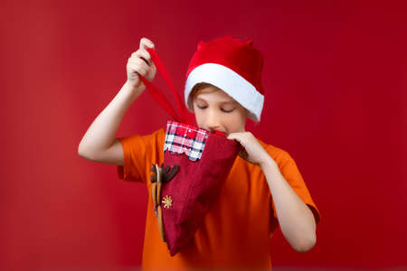 A boy in a Santa's Christmas hat looks into a gift bagの写真素材
