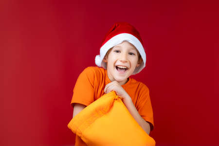 a cheerful boy in a Santa hat stuck his hand in a yellow Christmas bag and smilesの写真素材