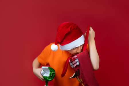 a boy on a red background in a yellow T-shirt and a Santa Claus hat pulled out a green hat from a gift bagの写真素材