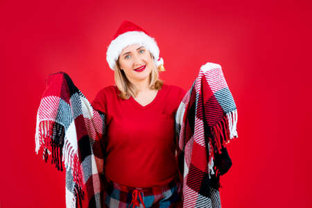 a woman on a red background in Christmas pajamas threw a blanket over herselfの写真素材