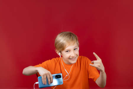 smiling boy on a red background holds a blue phone in his hand and shows different gesturesの写真素材