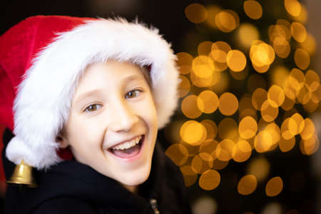 a laughing boy in a Santa hat on a beautiful blurred Christmas backgroundの写真素材