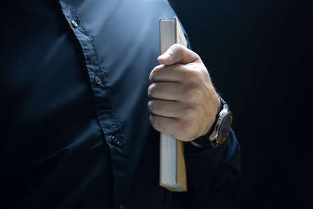 a man in black clothes keeps a thick book at his fingertie
