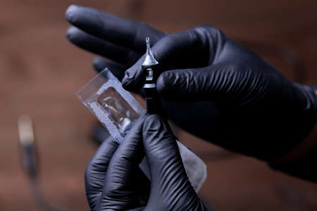 the hands of the permanent makeup artist in black medical gloves pulled a disposable cartridge out of the package and gently hold it with two fingersの写真素材