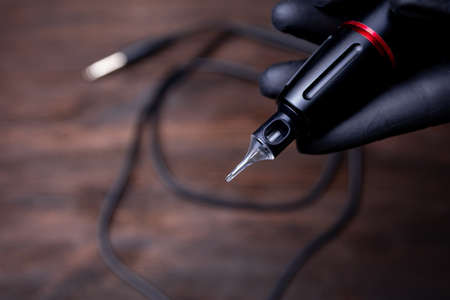 the hands of a permanent makeup artist in black sterile gloves shows a close-up of a tattoo machine...