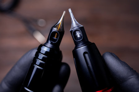 the hands of a permanent makeup artist in black sterile gloves holds two tattoo machines in his hands directing cartridges to each otherの写真素材