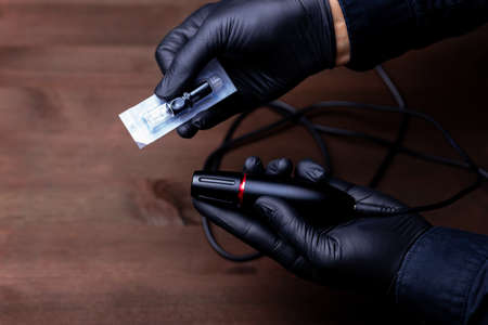 the hands of the permanent makeup master in black medical gloves took a disposable cartridge for tattooingの写真素材
