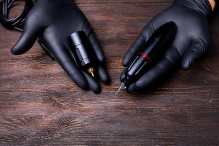 the hands of a permanent makeup artist in black sterile gloves on the palms of which there is a tattoo machine and a wireless unit for this machineの写真素材