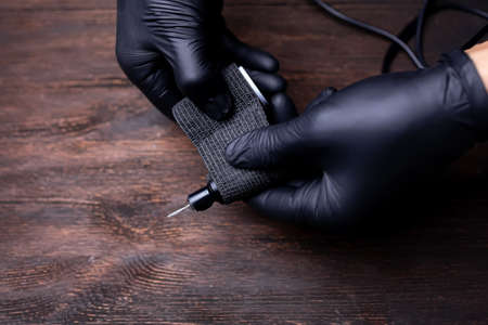 the hands of a permanent makeup artist in black sterile gloves stretch a black bandage tape to protect the tattoo machine wrapped around herの写真素材