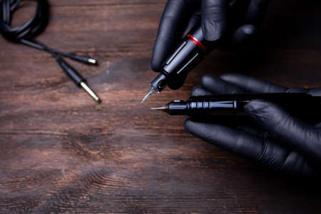 the hands of a permanent makeup artist in black sterile gloves holds two tattoo machines in his hands directing cartridges to each otherの写真素材