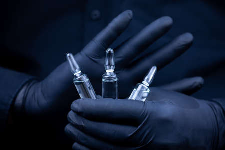 the doctor's hands in black medical gloves holds three vials of vaccine in front of him