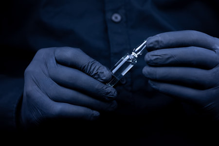 the hands of a doctor in black medical gloves who turns over an ampoule with a vaccineの写真素材