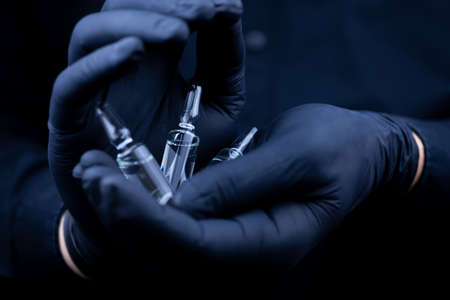 in the palms of the doctor, who is wearing black medical gloves, there are glass vials with a...