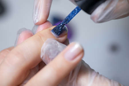 the master of the nail service makes a manicure to apply a blue gel polish with a nail brushの写真素材